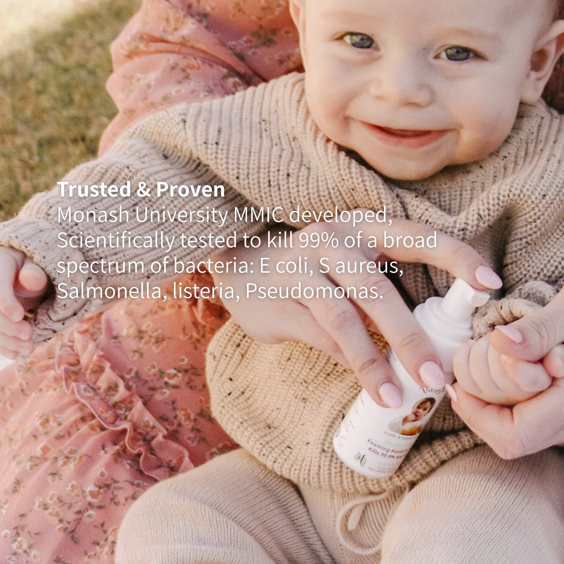Smiling Baby holding a bottle of kidsbliss hand sanitiser formulated with Monash University MMIC killing 99% bacteria.