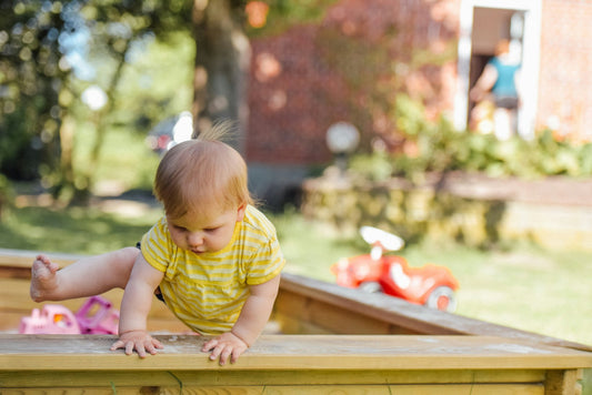 Baby playing outside in sandbox, reminding parents of year-round sunscreen protection.