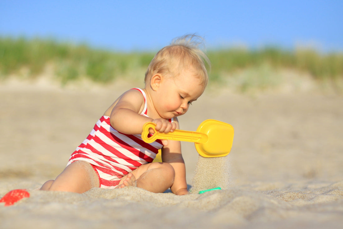 Baby playing in sand at the beach while wearing KidsBliss mineral sunscreen for kids.