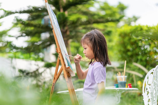 Child painting outdoors in a garden, enjoying creativity and nature.
